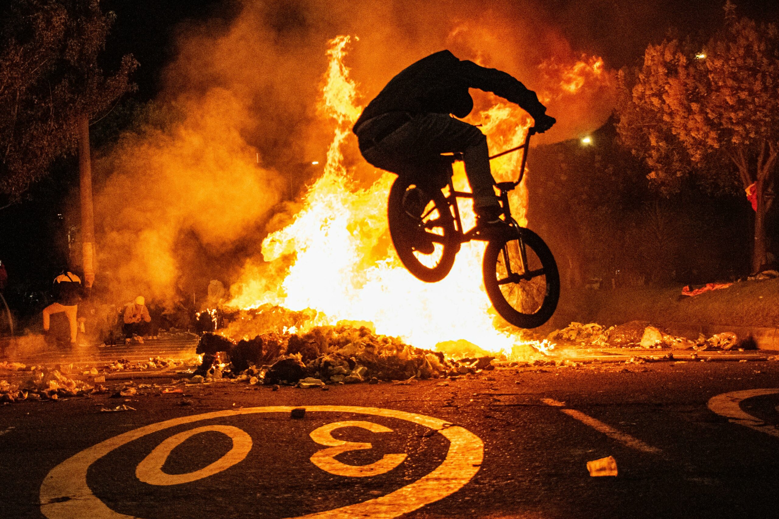 Silhouette of BMX biker performing a stunt over a blazing fire at night in Bogotá.