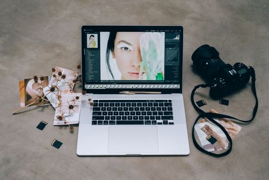 Why Your Gorgeous Portfolio Isn’t Getting You High-Ticket Clients (And What Will) A stylish photography setup with a laptop editing a portrait and a camera surrounded by SD cards on a concrete surface.